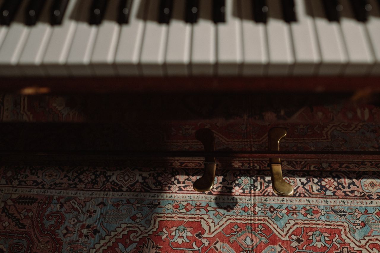 Artistic close-up of piano keys and pedals over vibrant patterned carpet in low light.